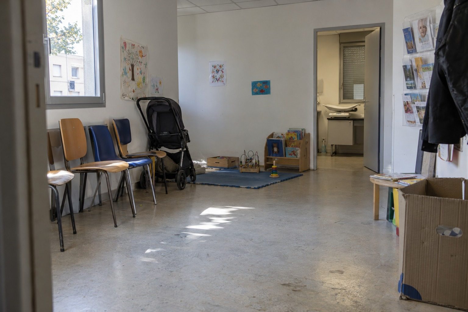 Salle d'attente vide d'un centre de PMI à Perpignan, avec poussette, coin jeux en bois et pèse-bébé au fond